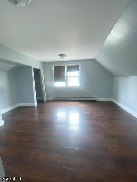 additional living space with lofted ceiling, a baseboard heating unit, and dark hardwood / wood-style floors