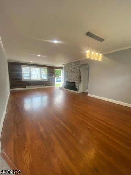 unfurnished living room featuring hardwood / wood-style flooring, a stone fireplace, and ornamental molding