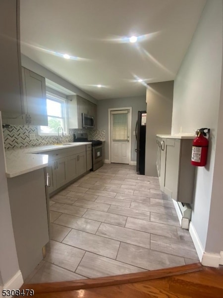 kitchen with gray cabinetry, stainless steel appliances, decorative backsplash, and light tile patterned floors