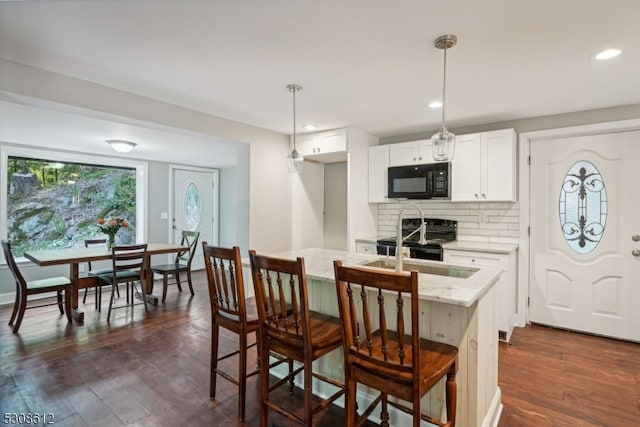 kitchen featuring a breakfast bar, white cabinetry, light stone counters, black appliances, and decorative light fixtures