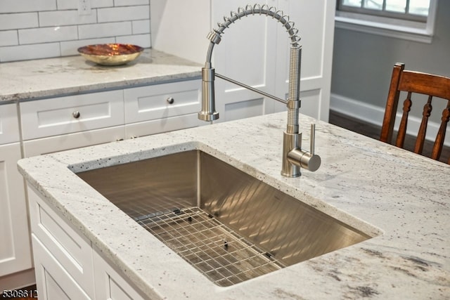 interior details with light stone counters, white cabinetry, sink, and decorative backsplash