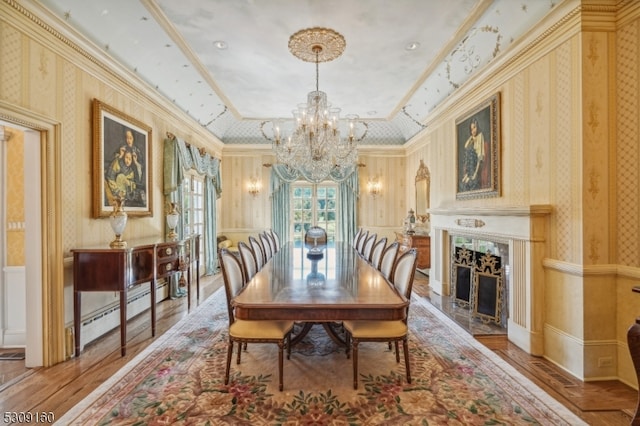 dining area with hardwood / wood-style flooring, a tray ceiling, ornamental molding, and a high end fireplace