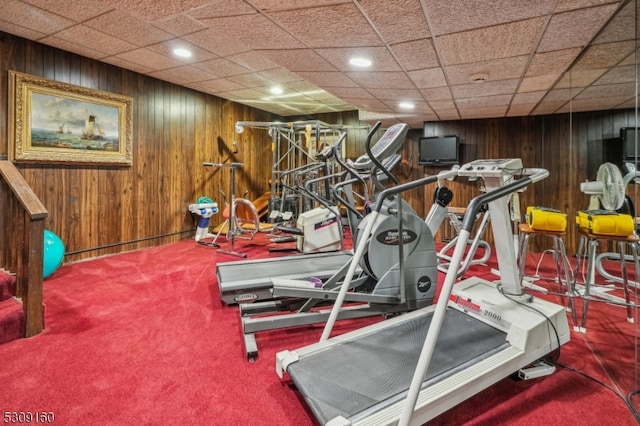 exercise area with wood walls, carpet floors, and a paneled ceiling