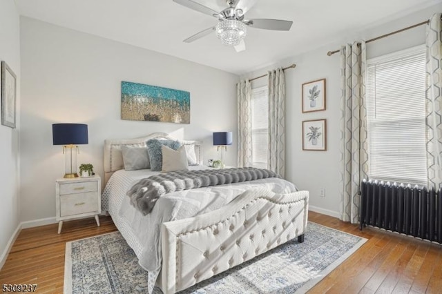 bedroom with a ceiling fan, baseboards, radiator heating unit, and wood finished floors