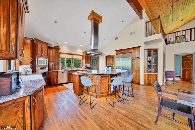 kitchen featuring built in appliances, light stone counters, a center island, island exhaust hood, and light hardwood / wood-style floors