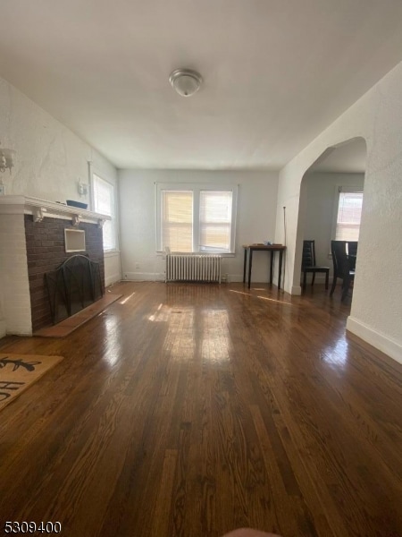 unfurnished living room featuring radiator, dark hardwood / wood-style flooring, and a brick fireplace