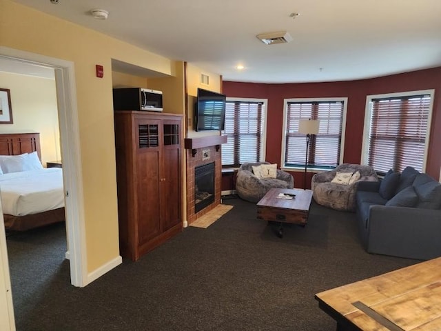 living room with dark colored carpet, a tiled fireplace, visible vents, and baseboards