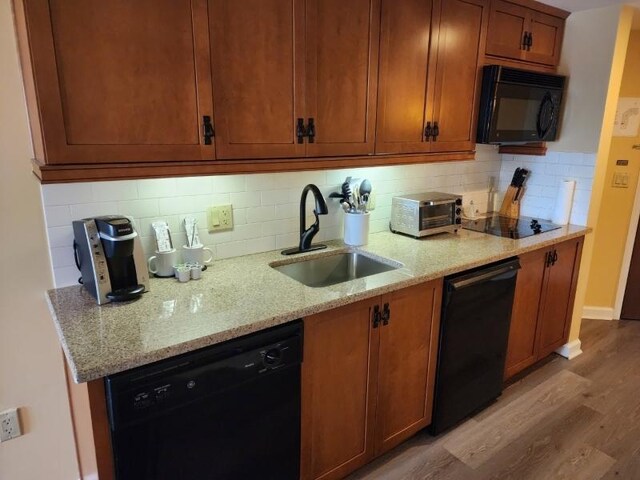 kitchen with black appliances, light hardwood / wood-style flooring, tasteful backsplash, sink, and light stone counters