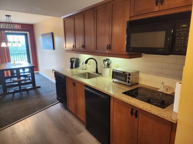 kitchen featuring light stone countertops, decorative light fixtures, black appliances, dark wood-type flooring, and sink