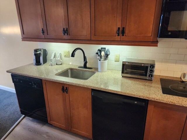 kitchen with black appliances, light stone counters, sink, decorative backsplash, and hardwood / wood-style flooring