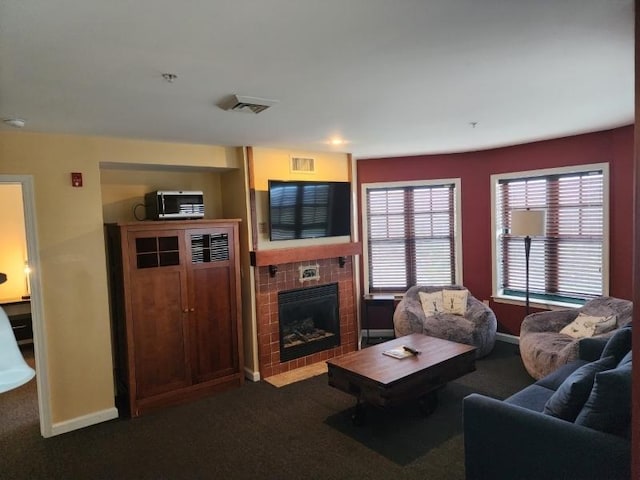 living room featuring dark carpet, visible vents, and a fireplace