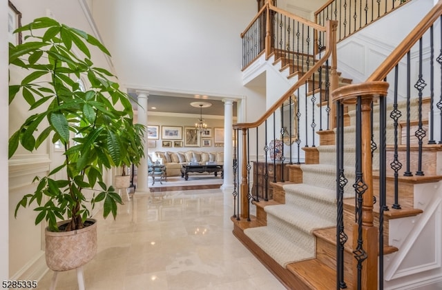 stairs with a towering ceiling, ornamental molding, ornate columns, and a notable chandelier