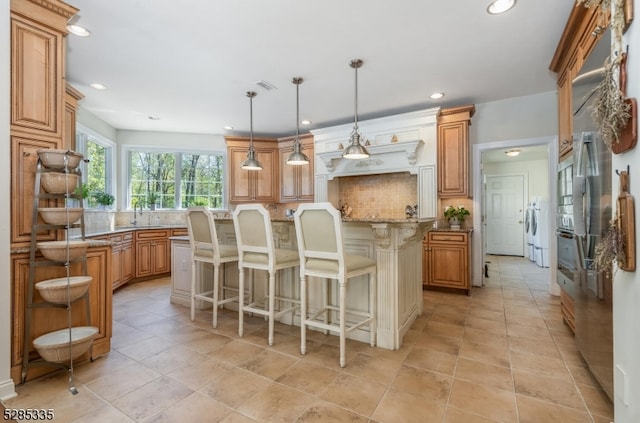 kitchen with a kitchen breakfast bar, decorative light fixtures, light stone countertops, sink, and decorative backsplash