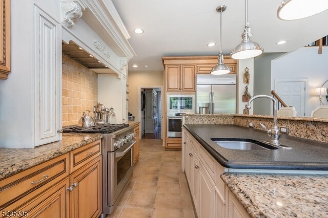 kitchen featuring dark stone countertops, custom range hood, sink, built in appliances, and tasteful backsplash