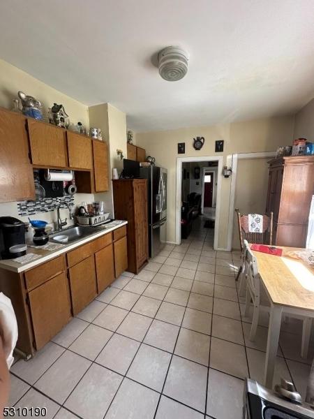kitchen with a sink, light countertops, light tile patterned floors, brown cabinets, and stainless steel refrigerator with ice dispenser