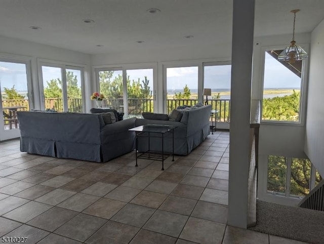 living room featuring dark tile patterned flooring, a water view, and an inviting chandelier