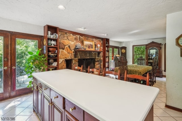 kitchen with a textured ceiling, light tile patterned flooring, a kitchen island, and a stone fireplace