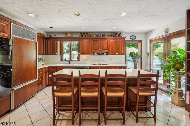 kitchen with paneled built in refrigerator, a kitchen island, a breakfast bar area, light tile patterned floors, and sink