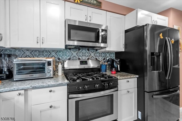 kitchen with appliances with stainless steel finishes, tasteful backsplash, light stone countertops, and white cabinets