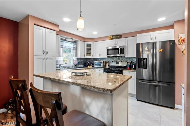 kitchen featuring tasteful backsplash, light stone counters, a kitchen island, appliances with stainless steel finishes, and white cabinets