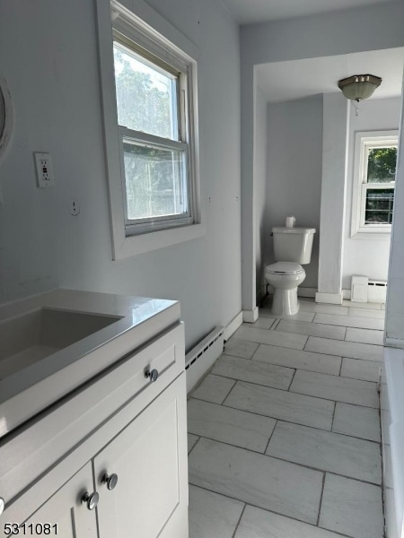 bathroom featuring vanity, toilet, baseboard heating, and a wealth of natural light