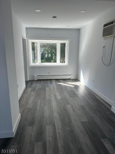 unfurnished room featuring dark wood-type flooring, a wall mounted AC, and baseboard heating