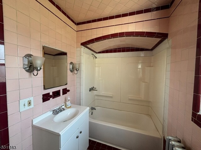 bathroom featuring tile patterned floors, vanity, radiator heating unit, tile walls, and  shower combination