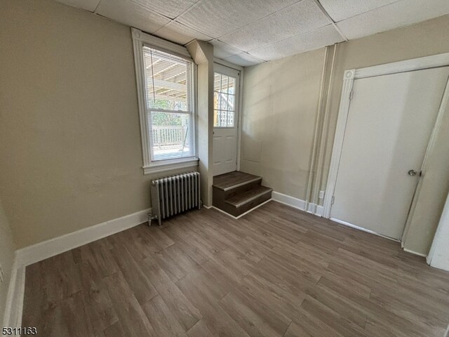 interior space with hardwood / wood-style floors, radiator heating unit, a drop ceiling, and a closet