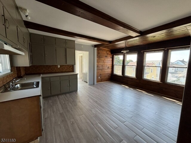 kitchen featuring light hardwood / wood-style flooring, sink, wood walls, decorative backsplash, and beam ceiling