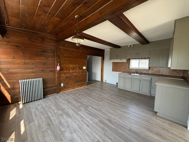 kitchen featuring light wood-type flooring, wooden walls, backsplash, radiator heating unit, and beam ceiling