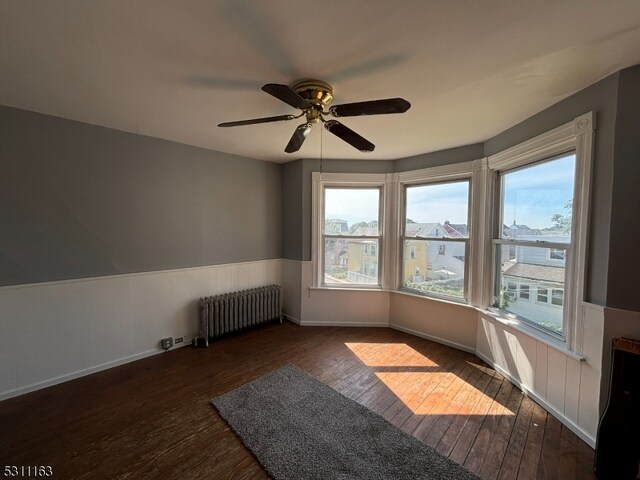 empty room with ceiling fan, dark hardwood / wood-style floors, and radiator heating unit