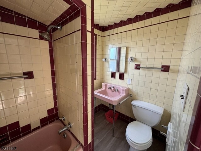 full bathroom featuring toilet, hardwood / wood-style floors, tiled shower / bath, sink, and tile walls