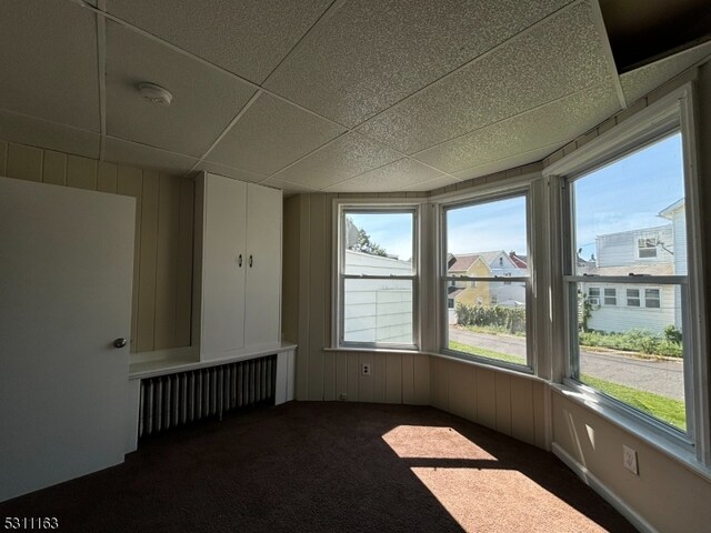 interior space with a paneled ceiling, radiator heating unit, and wood walls