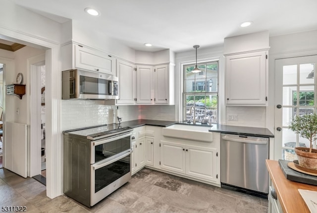 kitchen with a wealth of natural light, hanging light fixtures, appliances with stainless steel finishes, and white cabinets