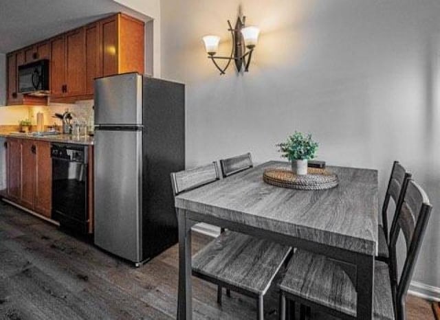 kitchen with dark wood-type flooring, brown cabinets, black appliances, and an inviting chandelier