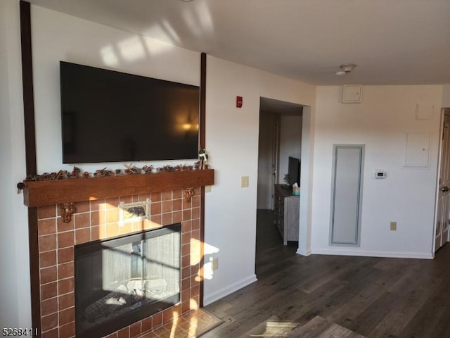 unfurnished living room featuring dark wood-style flooring, baseboards, and a tiled fireplace