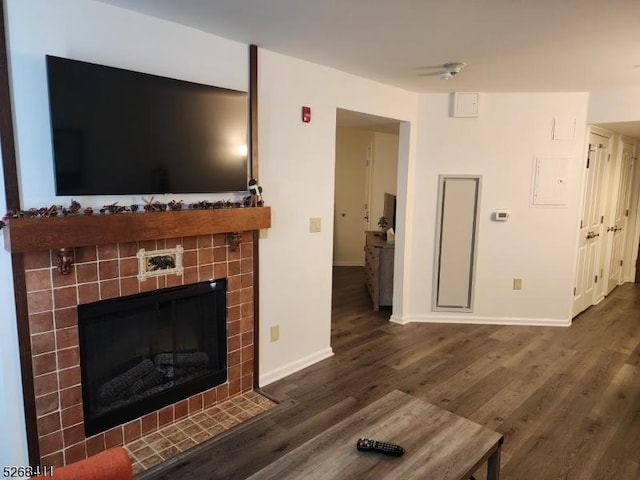 living room featuring a tile fireplace, dark wood finished floors, and baseboards