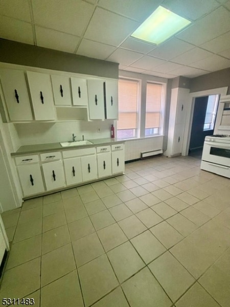 kitchen with light tile patterned floors, sink, white gas range oven, and white cabinets