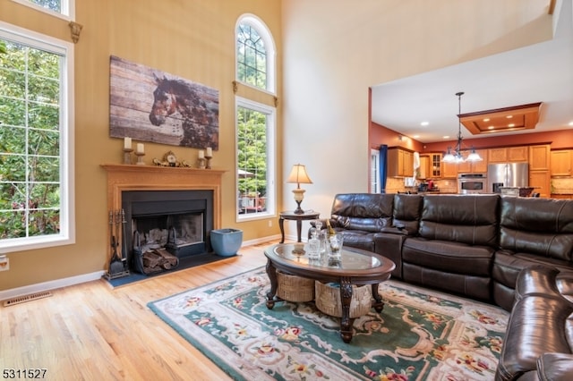 living room with light wood-type flooring, a raised ceiling, and a healthy amount of sunlight