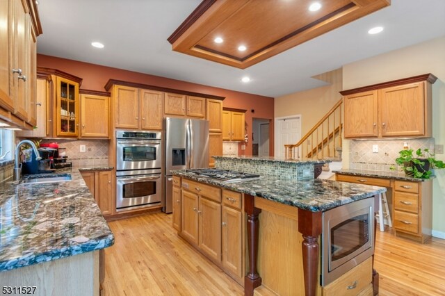 kitchen with appliances with stainless steel finishes, light hardwood / wood-style floors, a center island, sink, and dark stone countertops