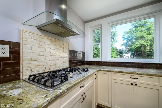 kitchen with stainless steel gas cooktop, light stone countertops, wall chimney exhaust hood, and vaulted ceiling