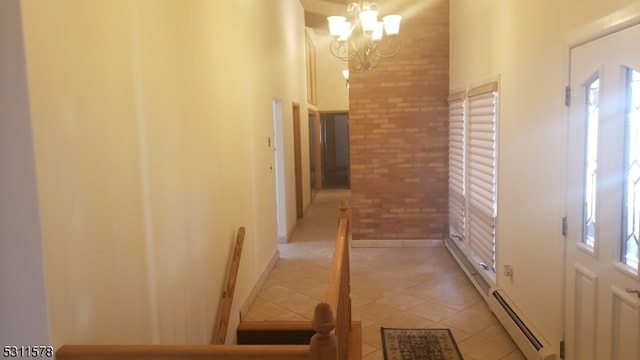 hall featuring light tile patterned floors, brick wall, a baseboard heating unit, and a chandelier