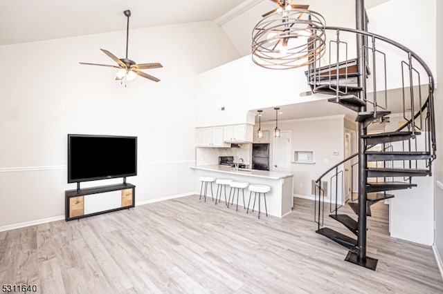 unfurnished living room with ceiling fan with notable chandelier, light hardwood / wood-style floors, and high vaulted ceiling