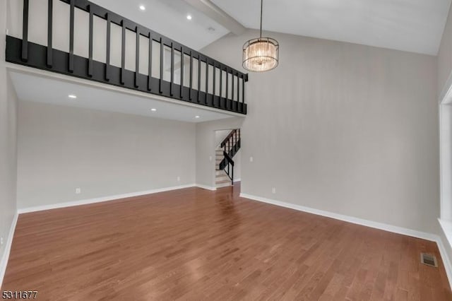 unfurnished living room with a chandelier, beamed ceiling, wood finished floors, stairway, and high vaulted ceiling