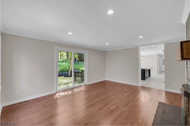 unfurnished living room featuring a fireplace, an inviting chandelier, crown molding, and light hardwood / wood-style flooring