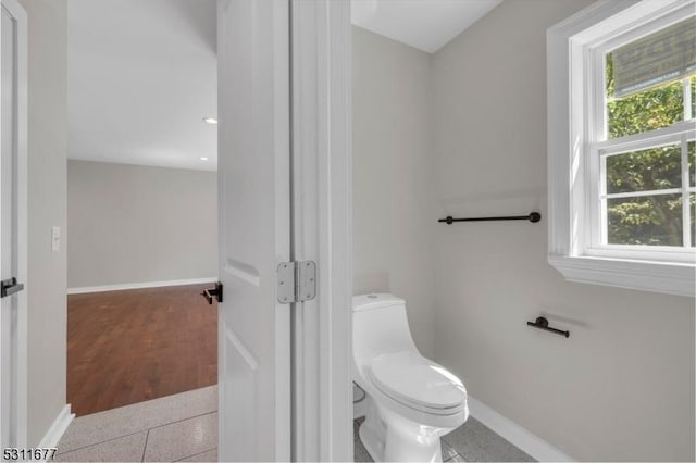 bathroom featuring toilet, a healthy amount of sunlight, and baseboards