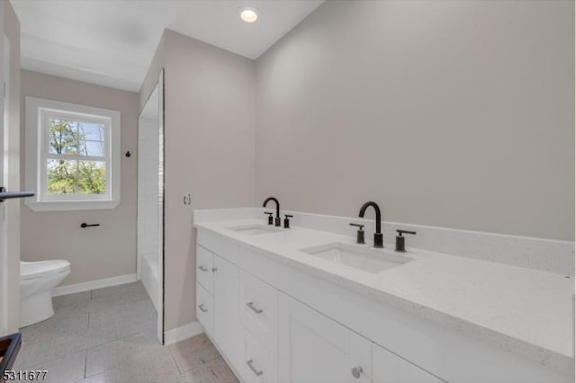 bathroom featuring toilet, a sink, double vanity, and baseboards