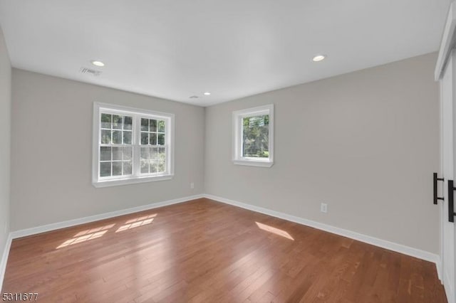 unfurnished room featuring baseboards, a healthy amount of sunlight, wood finished floors, and visible vents