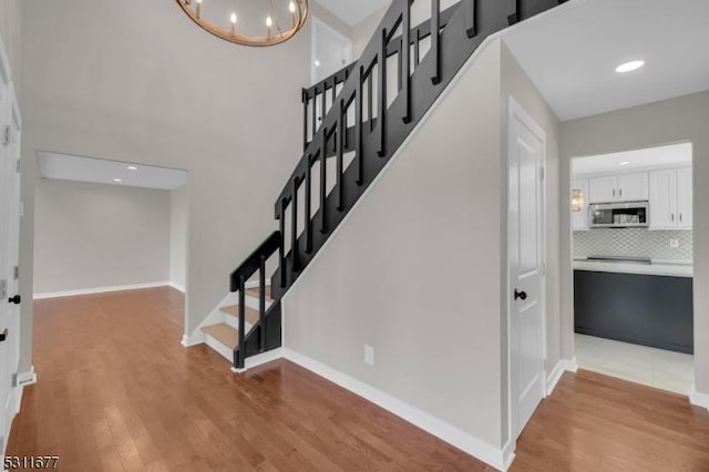 stairway featuring a towering ceiling, baseboards, wood finished floors, and an inviting chandelier