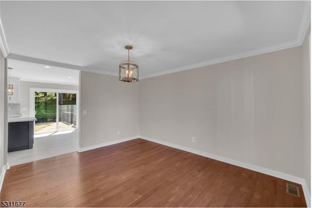 empty room with baseboards, wood finished floors, visible vents, and ornamental molding